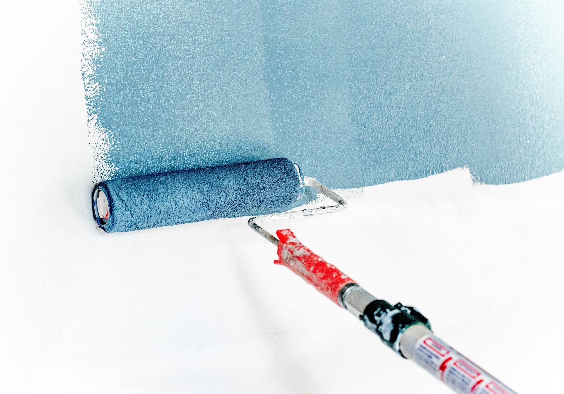 A paint roller applying blue paint to a white wall